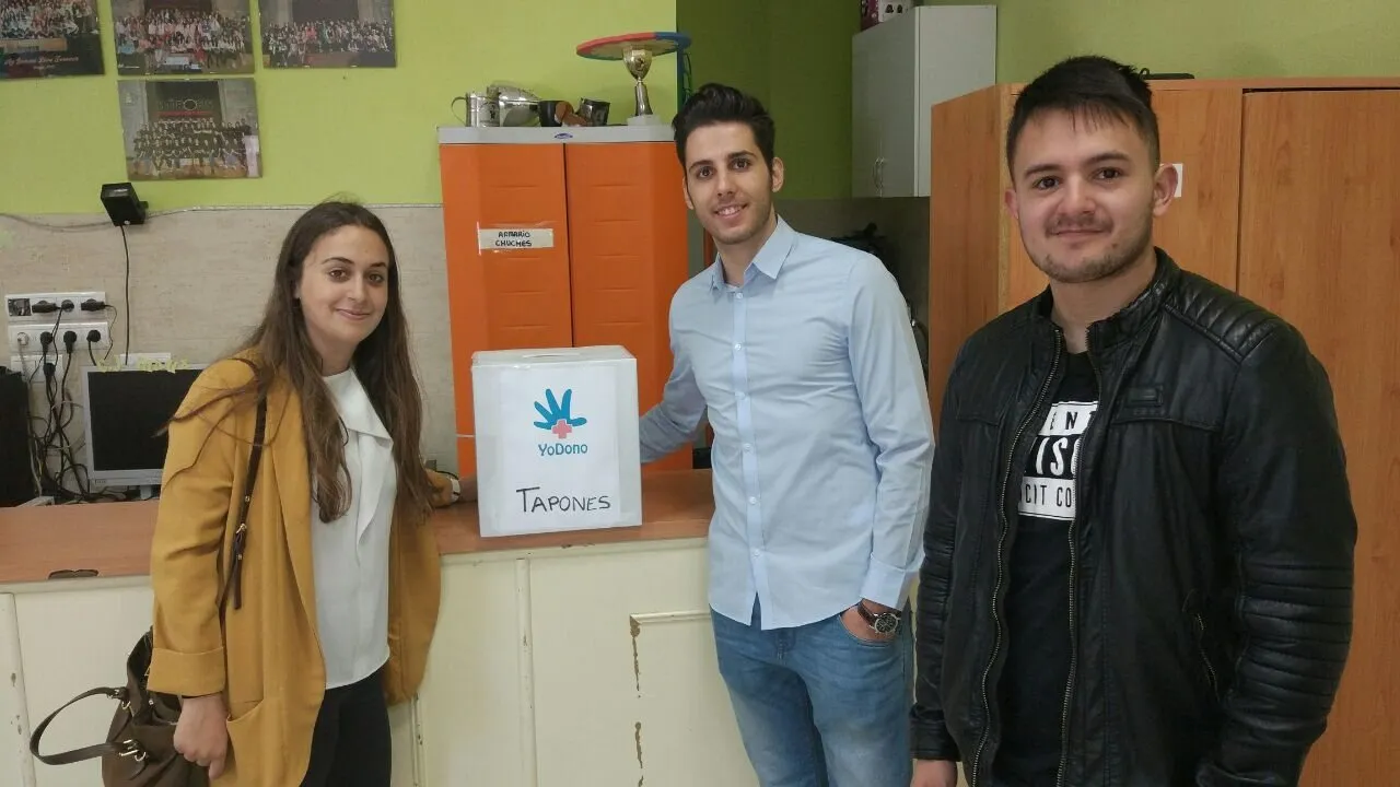 Tres de nosotros junto a una caja de donaciones de Yodono para recoger tapones.